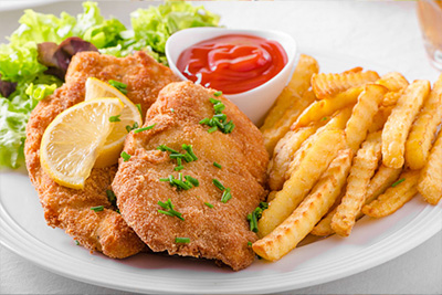 Schnitzel mit Pommes Ein Teller gefüllt mit zwei Stücken Wiener Schnitzel und Pommes, dazu Ketchup und Salat